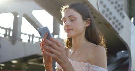 young brunette is calling by mobile phone on bridge in city and watching pictures on screen
