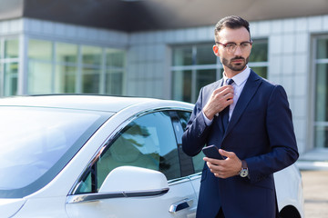 Prosperous businessman wearing glasses standing near his car