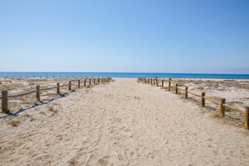 Fototapeta na wymiar wide sand pedestrian way with wooden banisters to Cabo de Gata Beach, wild and beautiful famous destination, in Almeria (Andalusia, Spain, Europe). Mediterranean sea in the horizon