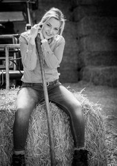 Junge, attraktive Landwirtin sitzt verträumt auf einem Strohballen in der Scheune
