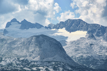 Wild mountain landscape with a glacier and clouds on a background of blue sky.