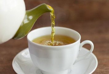 Hot green tea is poured into a white Cup on a wooden table
