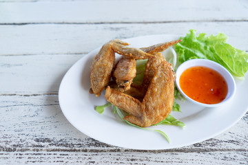 Fried chicken wings with chilli sauce in white plate on wooden background.