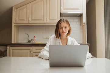 Worried woman working in kitchen in apartment with laptop looking at screen with astonishment. Concerned girl working at home on laptop. Freelancing concept.