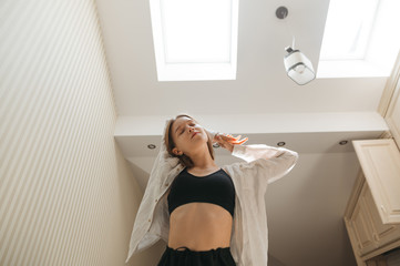 Portrait of attractive girl in casual clothes, morning exercise in apartment. Cute woman enjoys the morning with her eyes closed in the apartment with light interiors and skylights