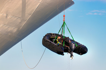 A sailor crew member is hanged with harness lowering a Rigid Hull Inflatable boat at sea.
