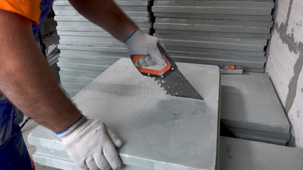 Repair in the apartment, a construction worker sawing plasterboard blocks