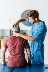 handsome bearded doctor touching head of middle aged patient in clinic
