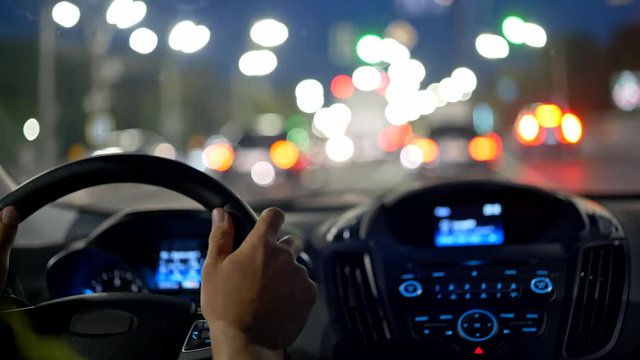 Man hands on steering wheel. Driving car in evening city through traffic jam