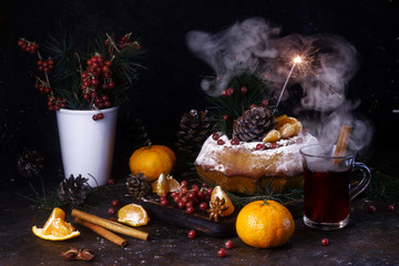 Fototapeta na wymiar Home made cake covered with powdered sugar and red berries. Burning sparkler, mulled wine, fir branches, fir cones and tangerines on a dark background.