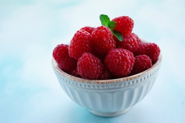 Fresh Raspberries in a bowl on blue background, selective focus