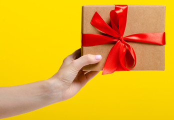 Gift box with red ribbon in hand on yellow background