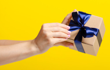 Gift box with blue ribbon in hand on yellow background
