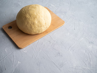 Dough in the shape of a ball on a cutting wooden Board, light concrete background.