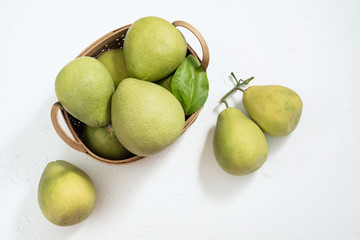 Fresh pomelo, grapefruit in bamboo basket with green leaf on bright white background. Seasonal fruit for Mid-Autumn Festival. Top view. Flat lay.