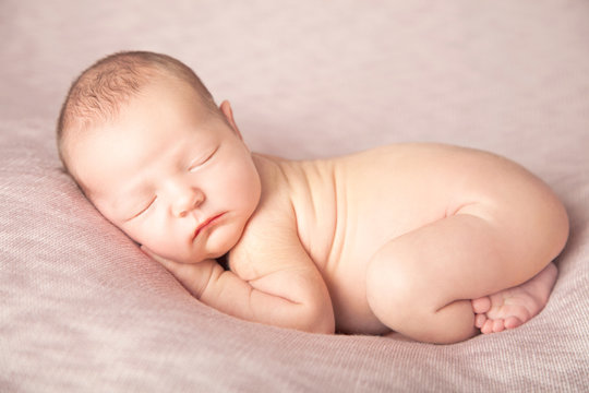 Newborn baby girl sleeping like a baby on a pink beanbag