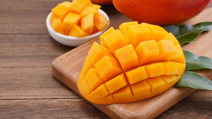Fresh mango, beautiful chopped fruit with green leaves on dark wooden table background. Tropical fruit design concept. Flat lay. Top view. Copy space