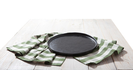 Black plate or tray, or pizza board, with tablecloth on wooden table. Top view mockup