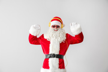 Portrait of cool Santa Claus listening to music on light background