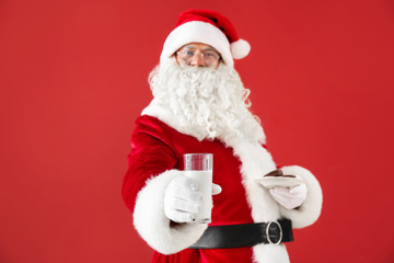 Santa Claus with milk and cookies on color background
