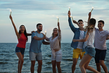 Obraz premium Happy friends with sparklers on sea beach at resort