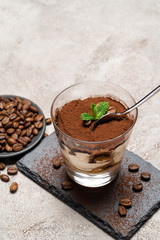 Portion of Classic tiramisu dessert in a glass cup on stone serving board on concrete background
