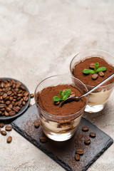 Portion of Classic tiramisu dessert in a glass cup on stone serving board on concrete background