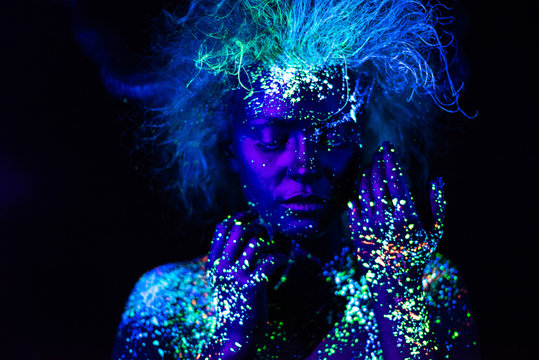 UV body art on the face of a very beautiful girl with a lush hairstyle on a dark background. Space figure.