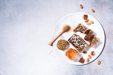 Honey products background. Honeycomb frame, bee pollen granules, honey in glass pot, almond nuts on grey concrete background. Copy space. Top view. Autumn harvest concept. Banner