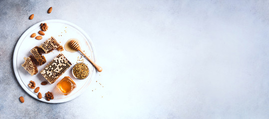 Honey products background. Honeycomb frame, bee pollen granules, honey in glass pot, almond nuts on grey concrete background. Copy space. Top view. Autumn harvest concept. Banner