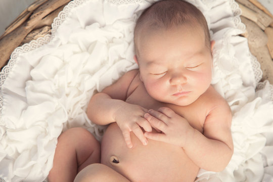 Close up of newborn baby face, asleep with hands on chest.