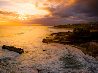 Dramatic sunset aerial over a black sand coastline with spray coming off the surf, Bali, Indonesia