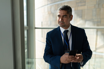 Fototapeta premium Mid-section of a businessman looking away and holding his mobile phone 