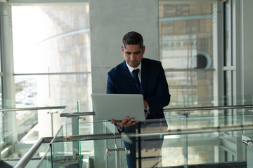 Front view of businessman leaned on the railing and working on his laptop in fisrt floor office 