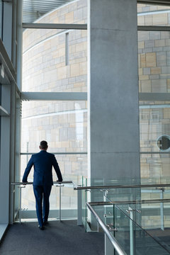 Rear view of businessman standing on the first floor of office and leaned on the railing looking thr
