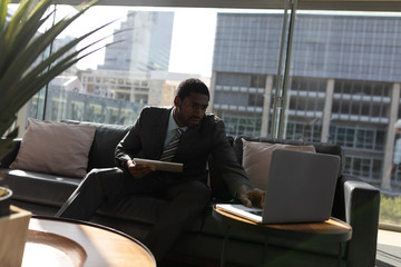 Fototapeta na wymiar African-American businessman with digital tablet working on laptop on sofa in office