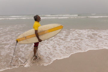 Senior male surfer with surfboard standing on the beach
