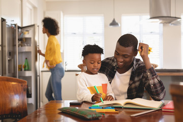 African American father helping his son with homework at table