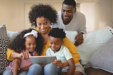 African American mother with her children using digital tablet on sofa while father looking them