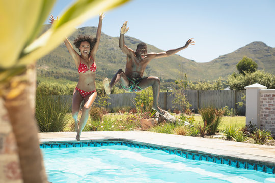Happy young African American couple jumping in a swimming pool in their backyard