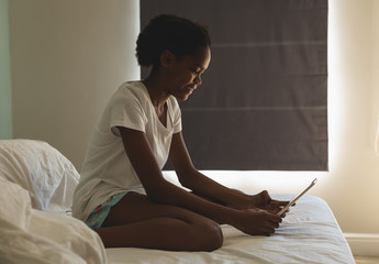 Happy African American girl using digital tablet on bed in bedroom