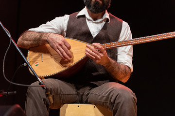 Good-looking man with a thick black beard, hands of musician playing a typical stringed instrument...