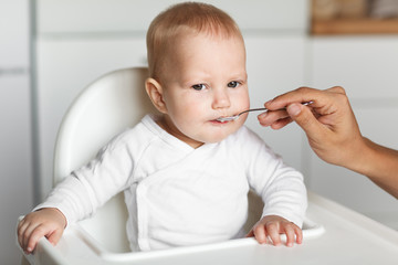 Feeding of cute baby with a spoon in the kitchen