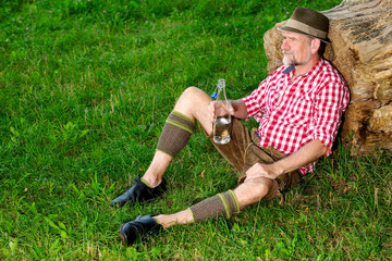 handsome bavarian man sitting outdoors at tree stump and drinking water