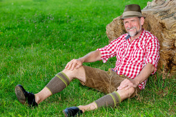 bavarian man sitting outdoors at tree stump and smiles