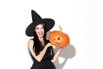 Young brunette woman in black hat and costume on white background. Attractive caucasian female model. Halloween, black friday, cyber monday, sales, autumn concept. Holding pumpkin. Looks happy.
