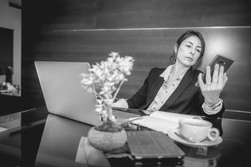 Fototapeta na wymiar Black and white photo of an attractive young businesswoman working in the office with laptop, cell phone and notebook and with a cup of coffee, with elegant wooden background