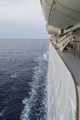 Weiße Bordwand mit Fenstern und Rettungsbooten und Deck von Kreuzfahrtschiff auf See