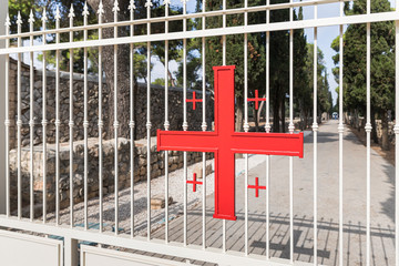 Fototapeta na wymiar A large metal cross of red color is attached to the gate to the catholic Christian Transfiguration Church located on Mount Tavor near Nazareth in Israel