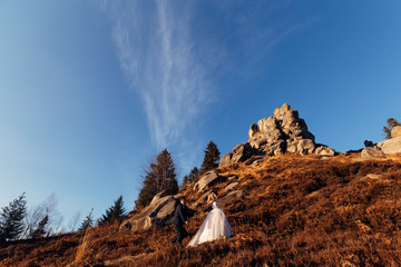 the bride holds the groom's hand and they go up the hill with cliff. nature.